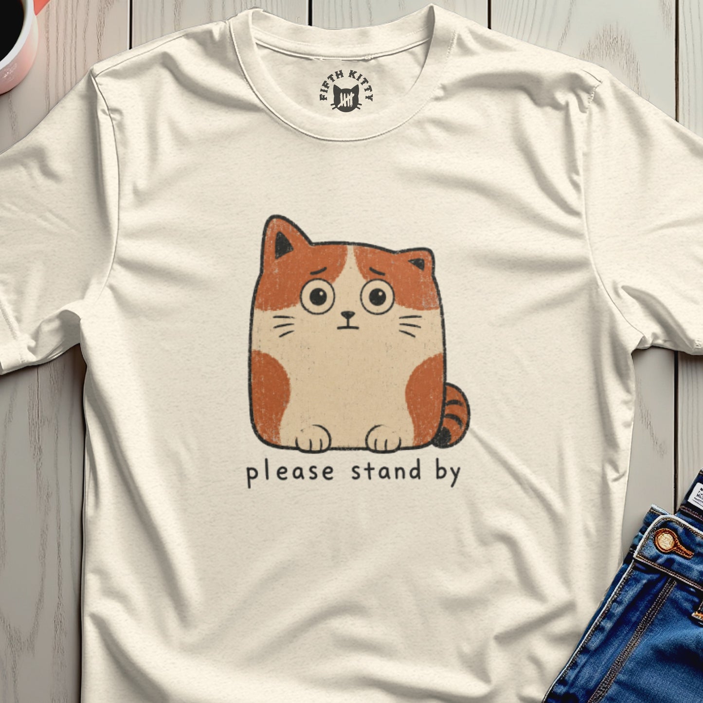 Cream t-shirt with a worried cartoon cat graphic and text "please stand by".