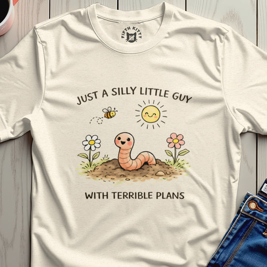 Cream t-shirt with cartoon worm, bee, sun, and flowers, saying "Just a silly little guy with terrible plans".