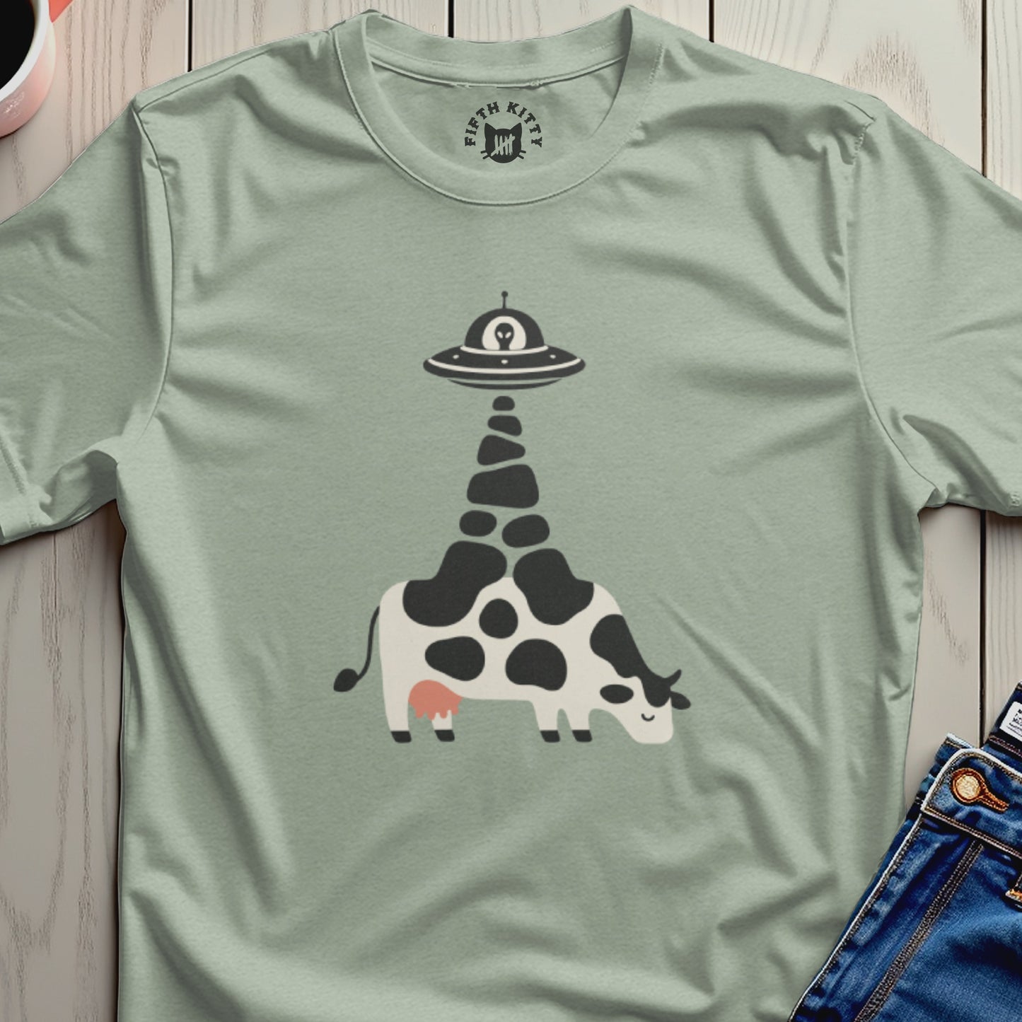 Cow with UFO abduction design on light green t-shirt.