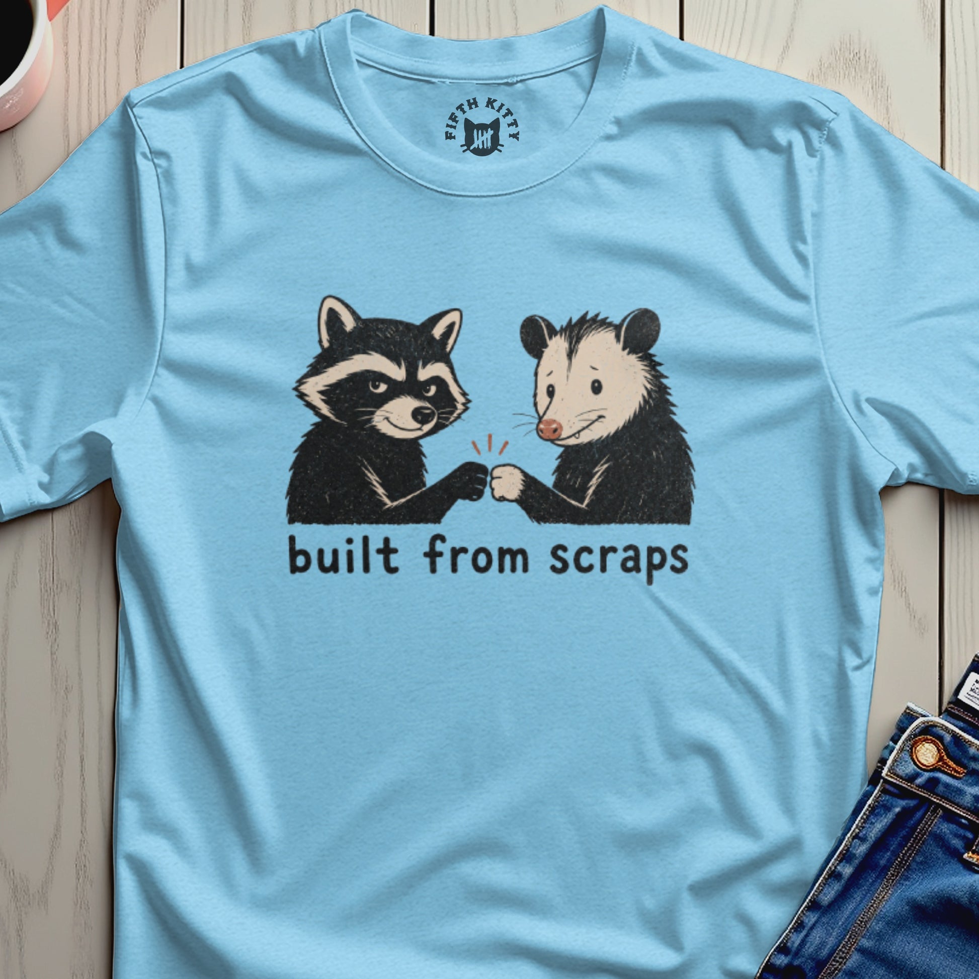 Light blue t-shirt with raccoon and opossum fist-bumping, text "built from scraps".