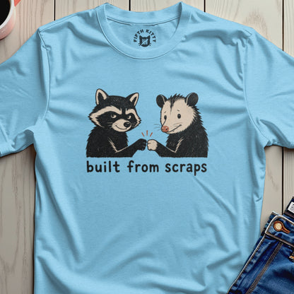 Light blue t-shirt with raccoon and opossum fist-bumping, text "built from scraps".