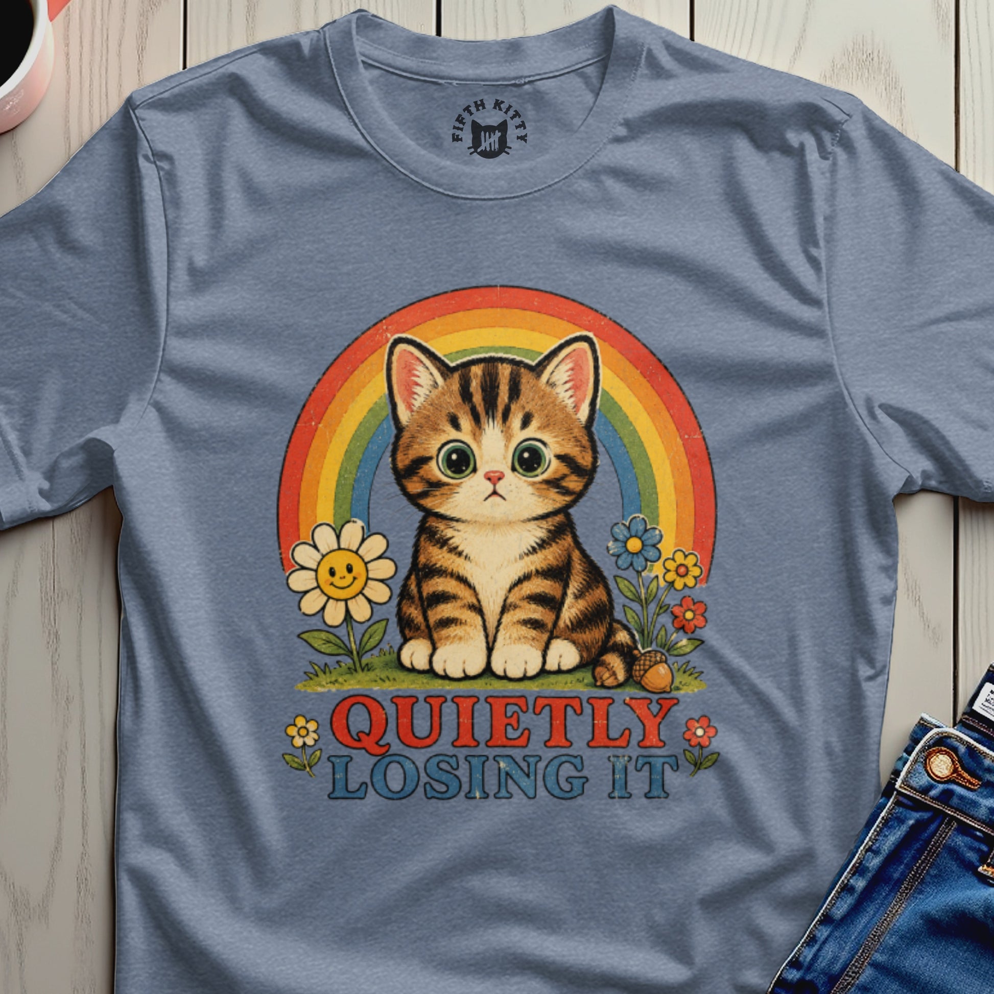 Tabby kitten with large eyes sits in front of a rainbow and flowers, text reads "Quietly Losing It".