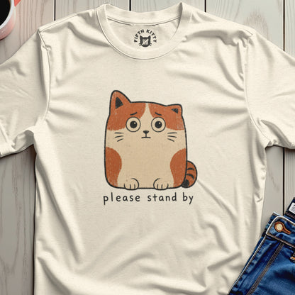 Cream t-shirt with a worried cartoon cat graphic and text "please stand by".