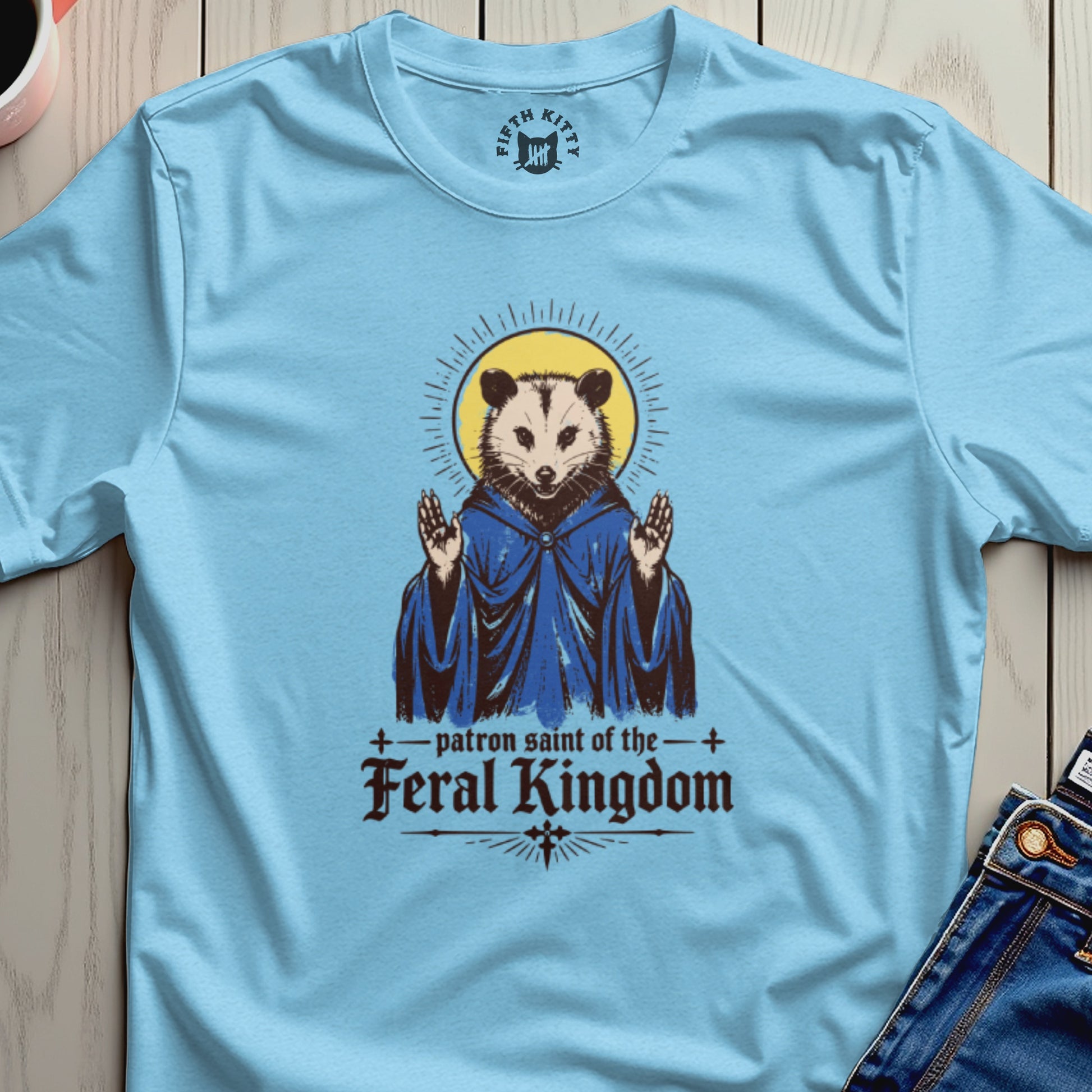 Opossum in blue robe, hands raised, with text "patron saint of the feral kingdom".
