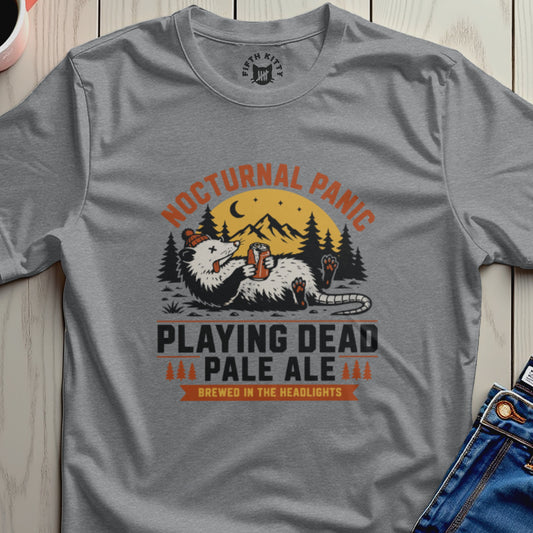 Gray t-shirt with 'Nocturnal Panic Playing Dead Pale Ale' graphic design on a wooden surface.