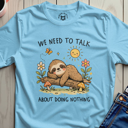 Light blue t-shirt with a sleeping sloth on a log, sun, flowers, and mushrooms.