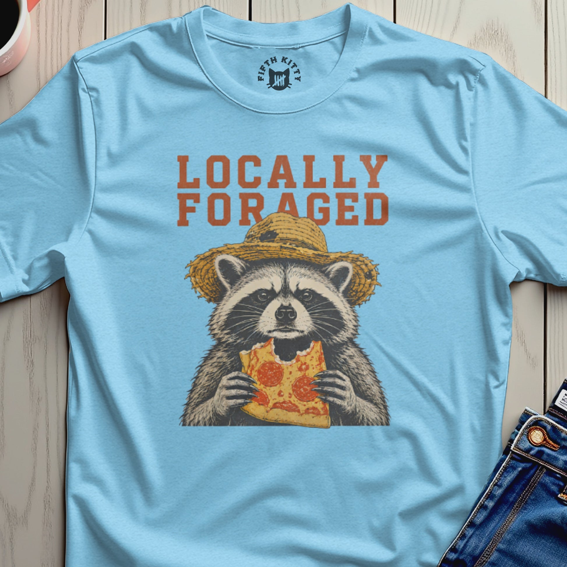 Light blue t-shirt with a raccoon wearing a straw hat eating pizza.