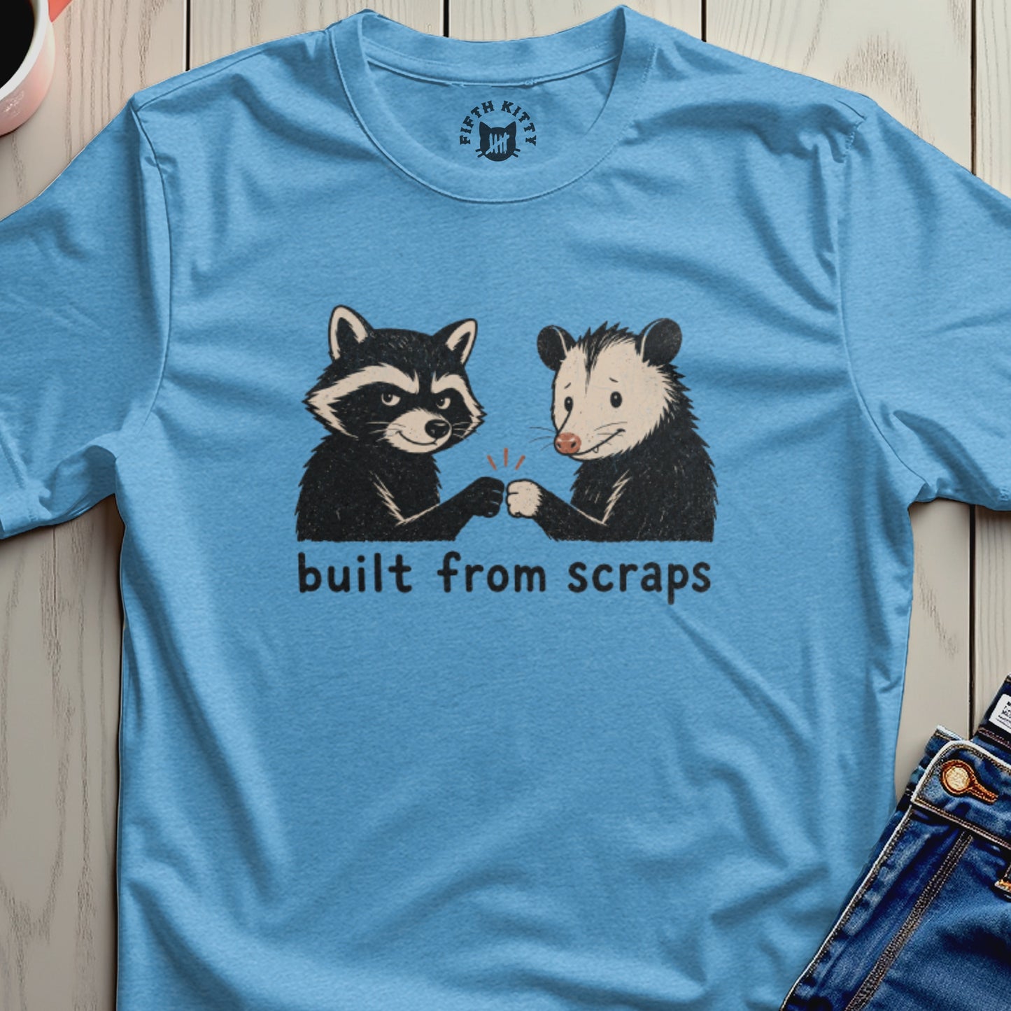 Blue t-shirt with raccoon and opossum fist bumping and text "built from scraps".