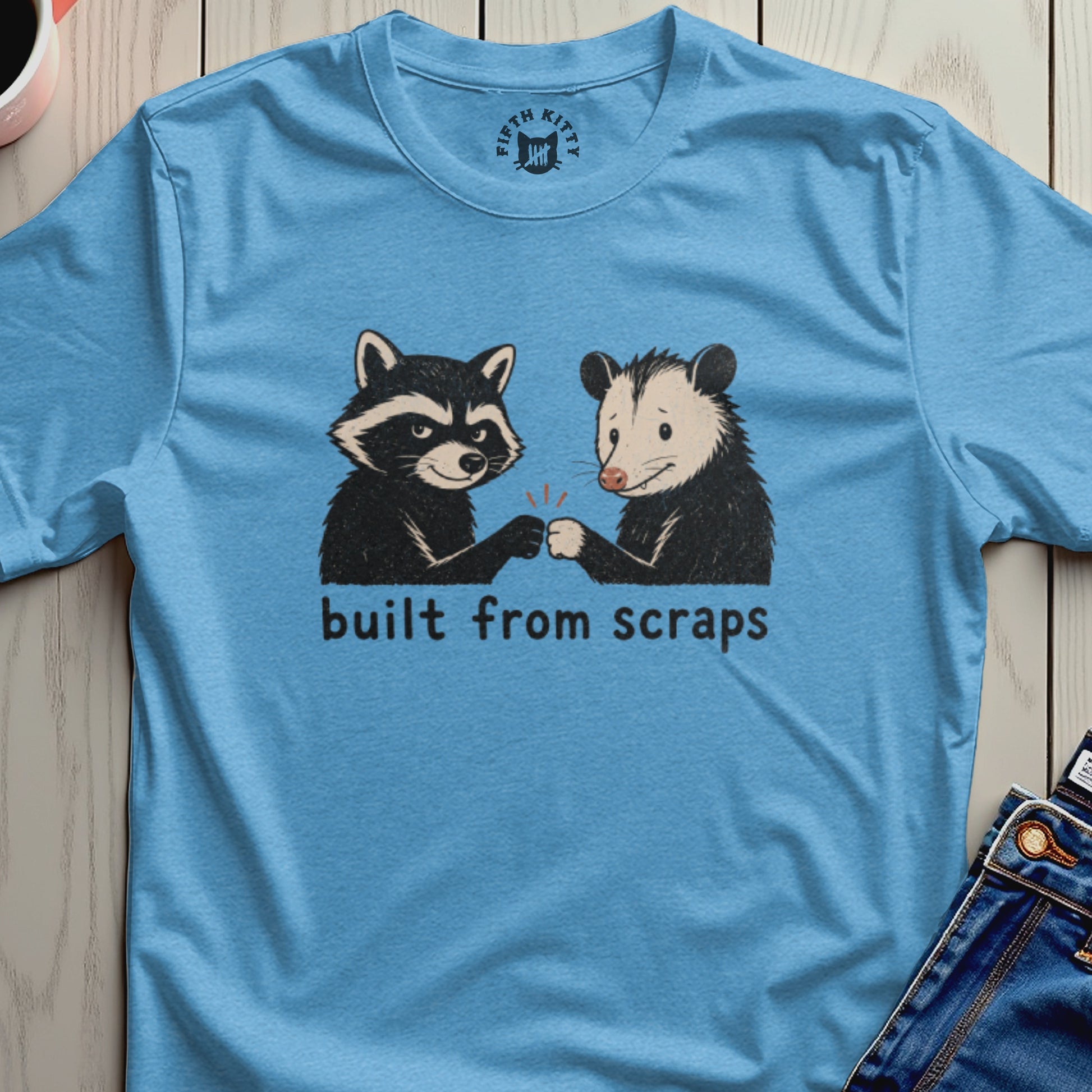 Blue t-shirt with raccoon and opossum fist bumping and text "built from scraps".