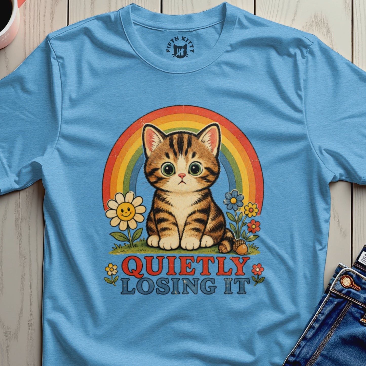 Blue t-shirt with a cartoon cat, rainbow, flowers, and text "QUIETLY LOSING IT".