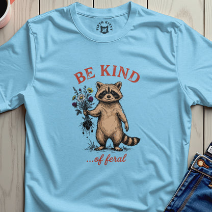 Light blue t-shirt with a raccoon holding flowers and the text "BE KIND ...of feral".