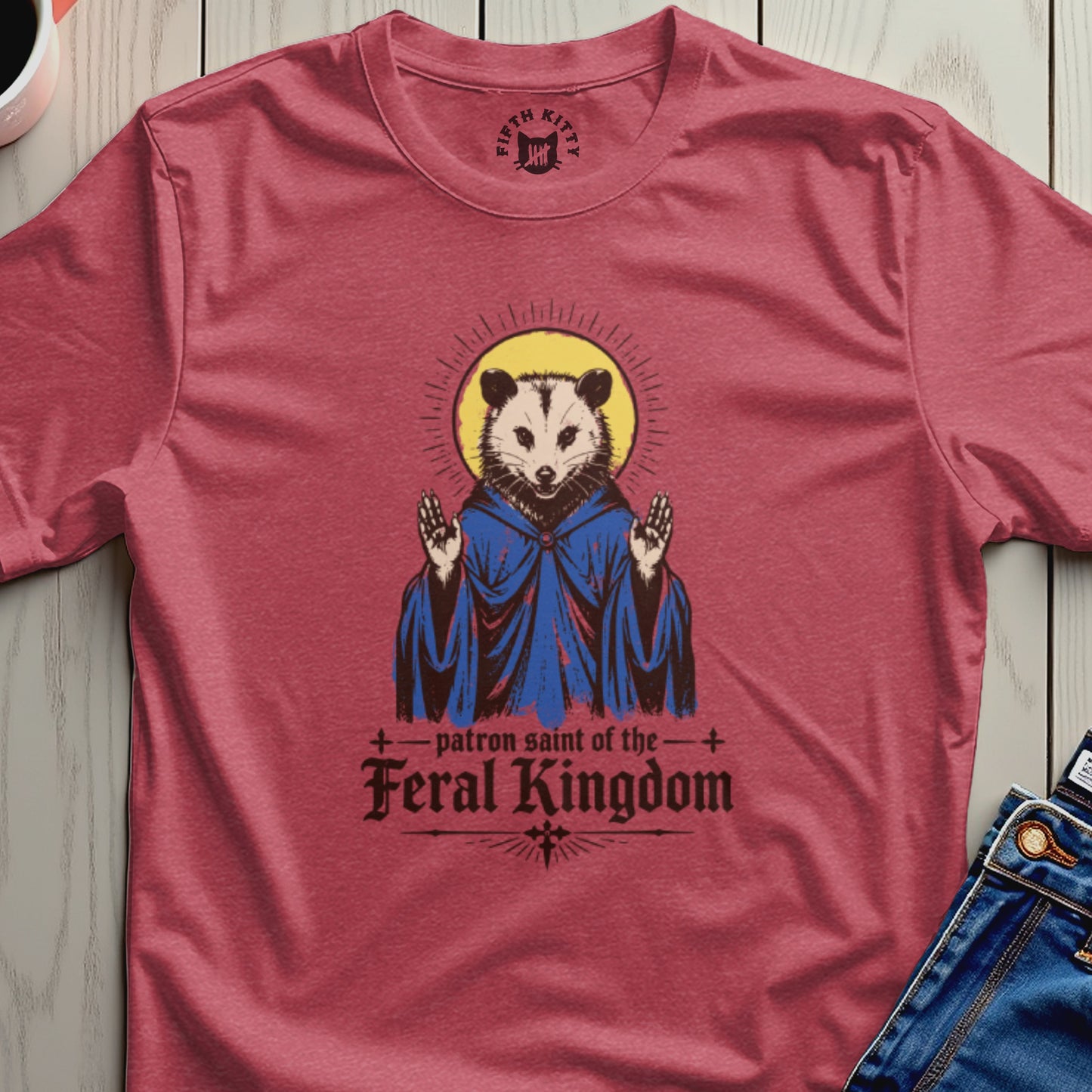 T-shirt featuring a possum in religious robes, with text "Patron Saint of the Feral Kingdom".