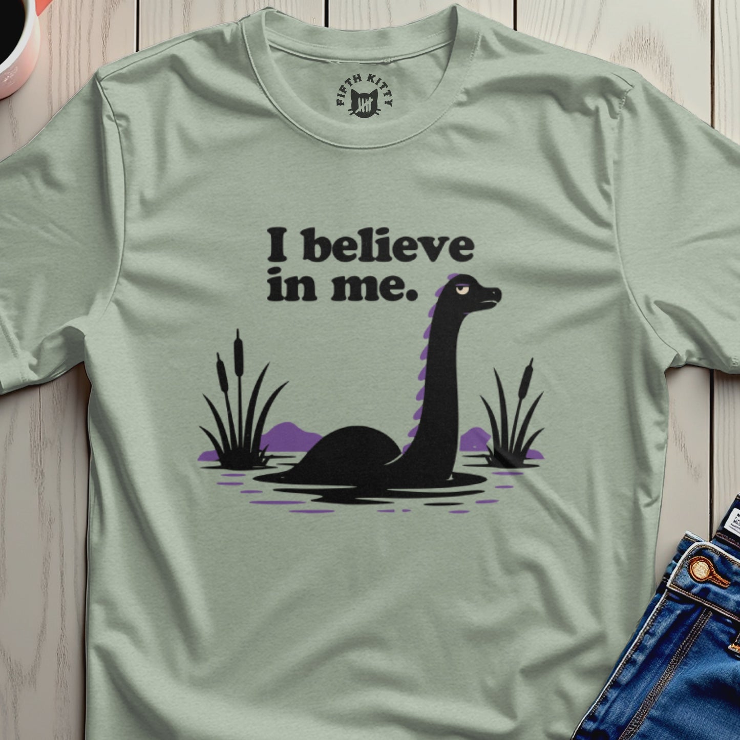 Green t-shirt with black text "I believe in me" and a cartoon monster.
