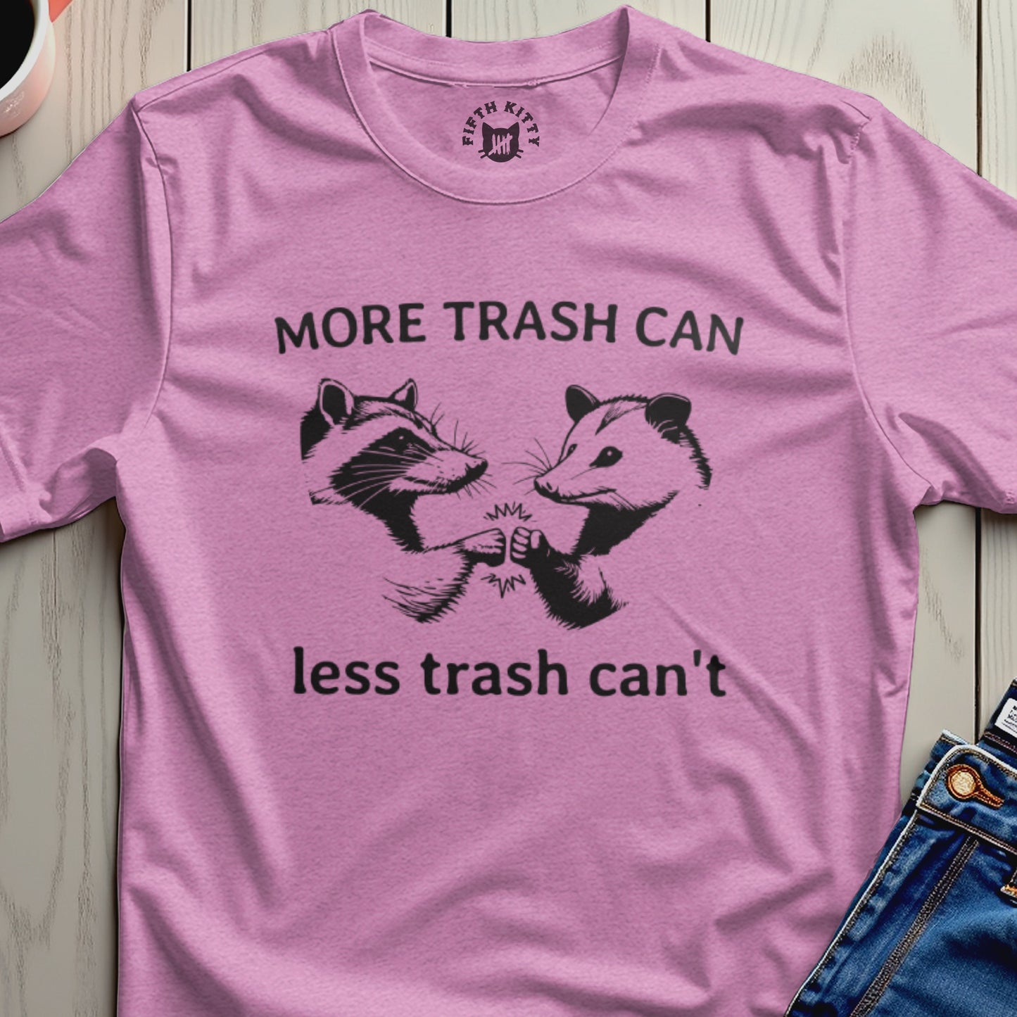 Pink t-shirt with raccoons and opossums fist bumping with text "MORE TRASH CAN less trash can't".