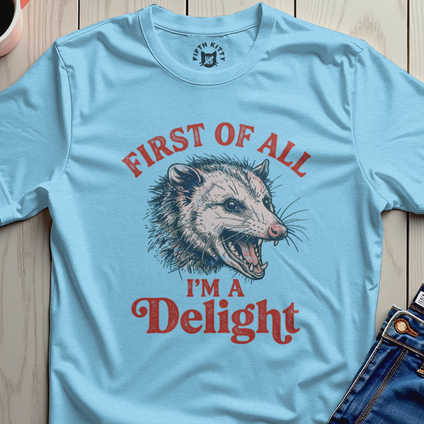 Light blue t-shirt with a distressed illustration of a possum and text "FIRST OF ALL I'M A DELIGHT".