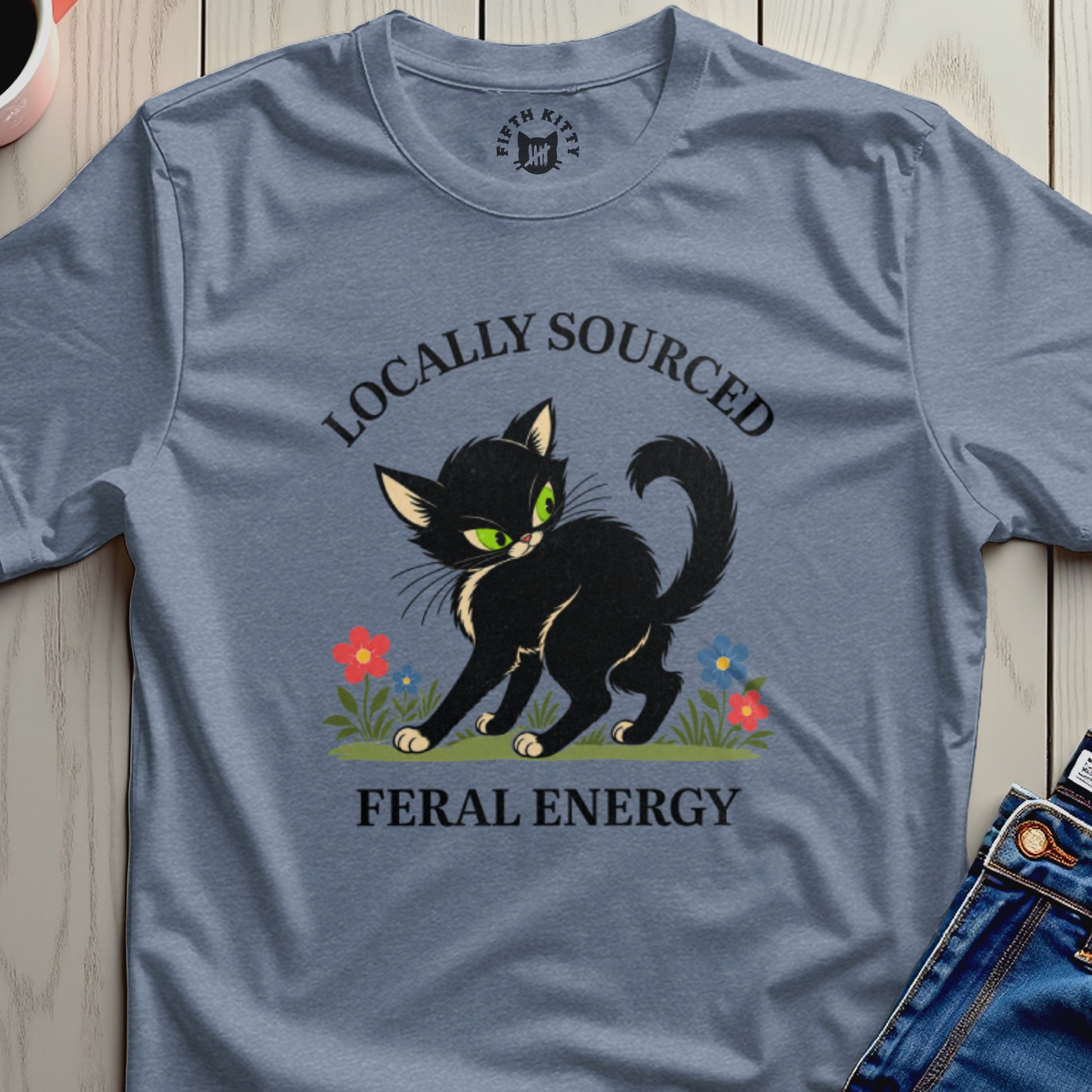 Black cat with green eyes on a blue t-shirt, "Locally Sourced Feral Energy."