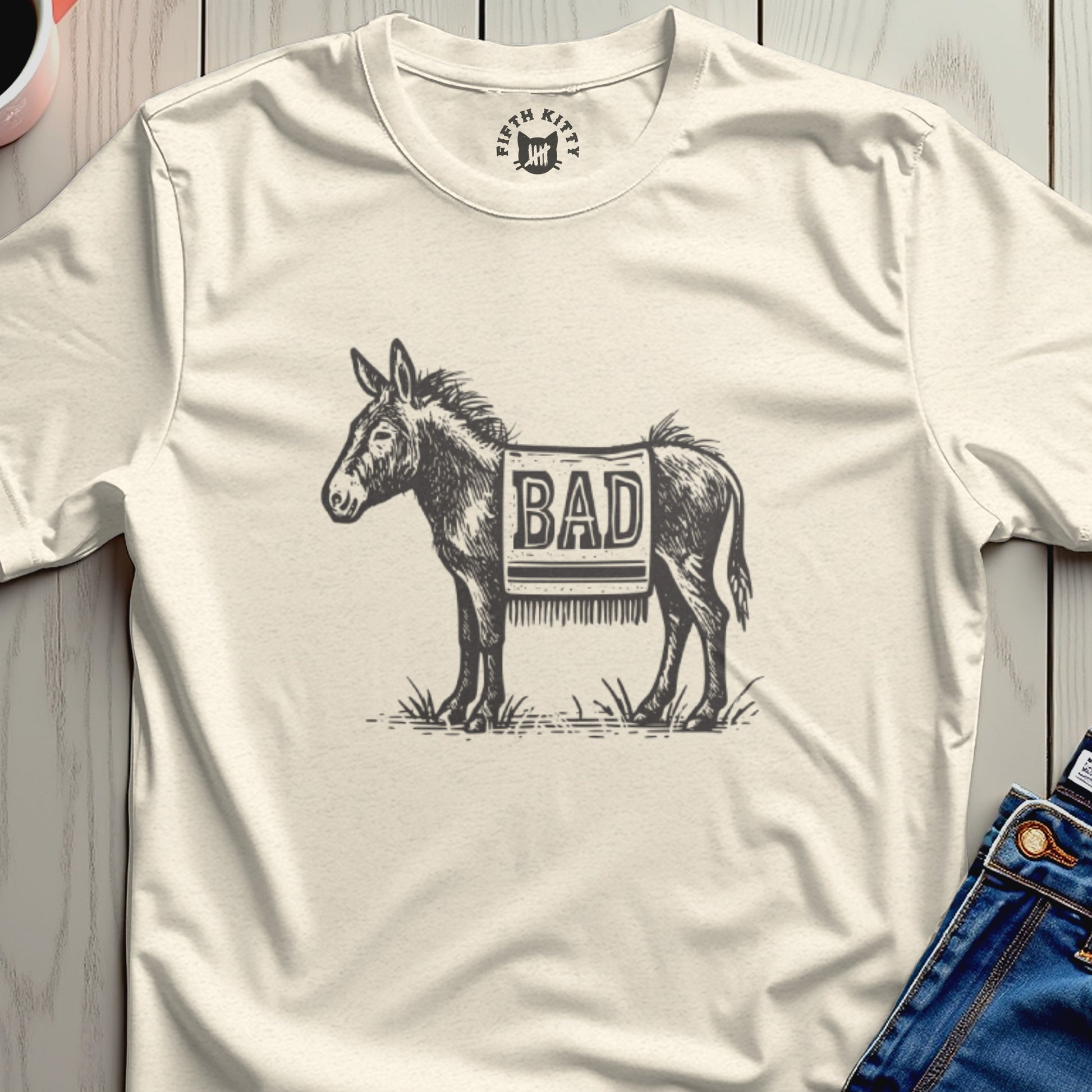 Cream t-shirt with a drawing of a donkey wearing a patterned blanket with "BAD" written on it.