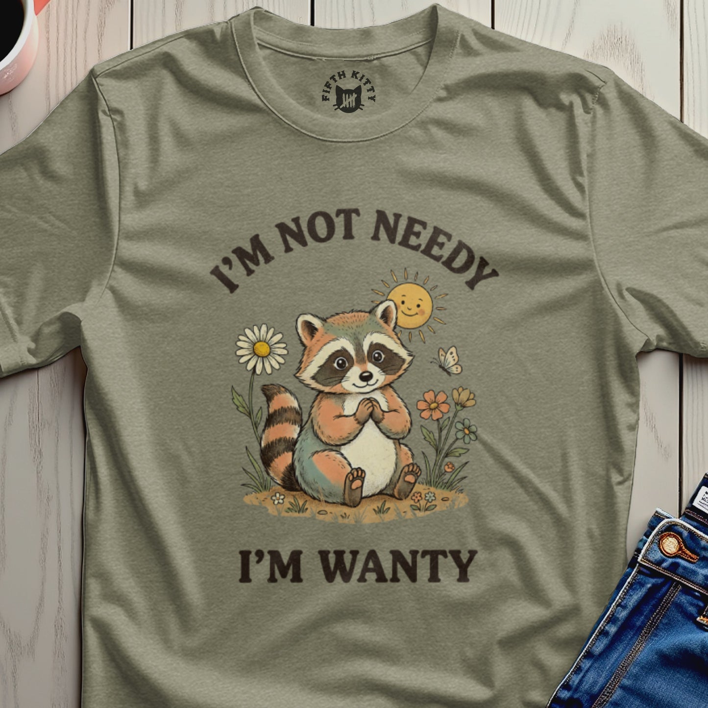 T-shirt with a smiling raccoon, sun, flowers, and text "I'M NOT NEEDY I'M WANTY".