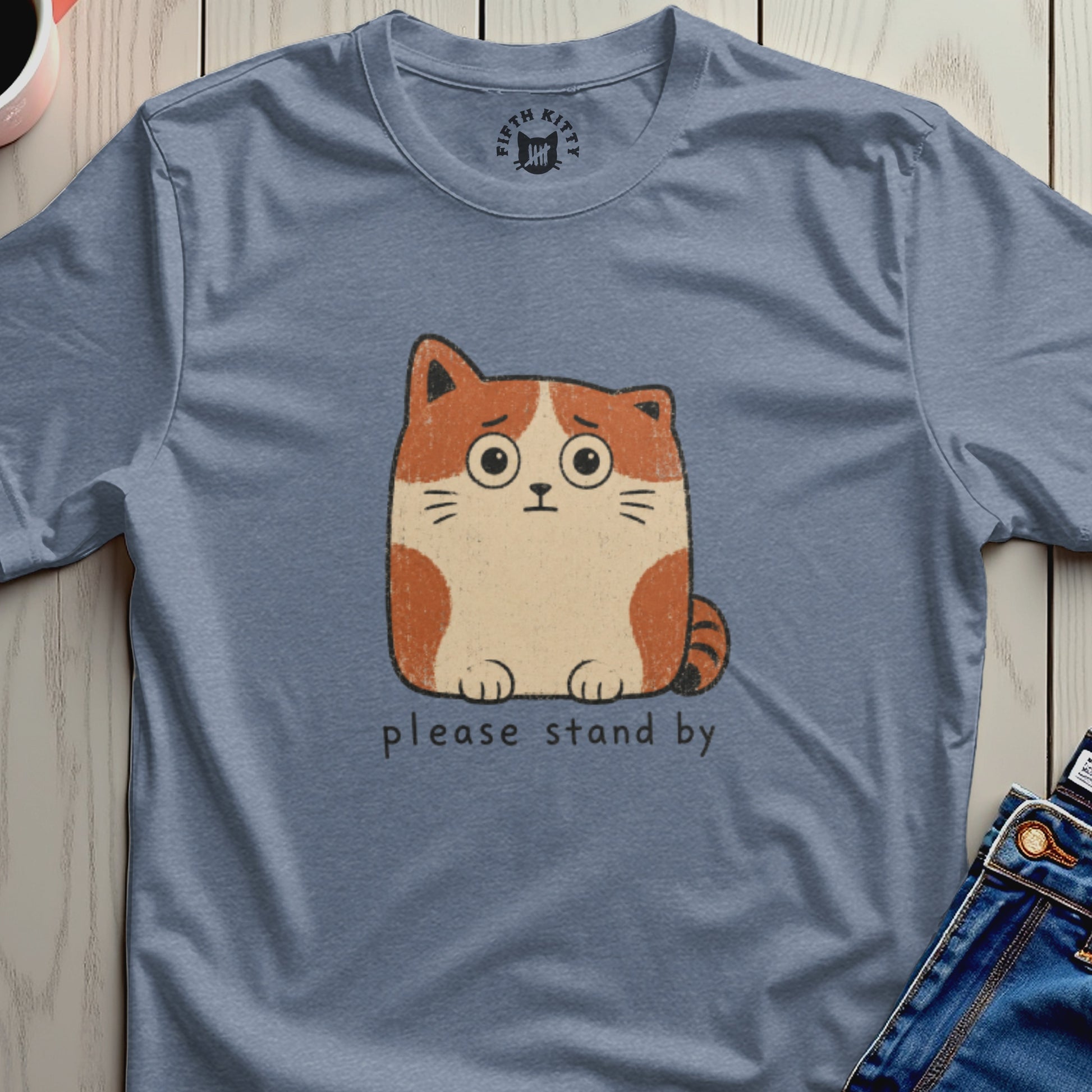 Blue t-shirt with anxious cartoon cat graphic saying "please stand by"