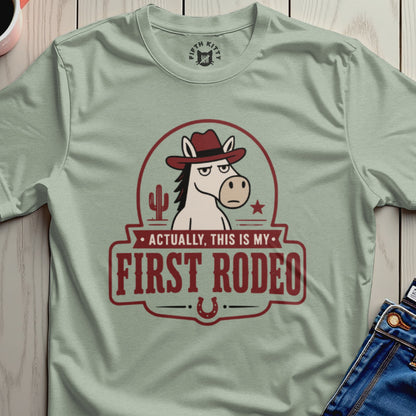Light green t-shirt with a cartoon horse wearing a cowboy hat and the text "Actually, this is my first rodeo."