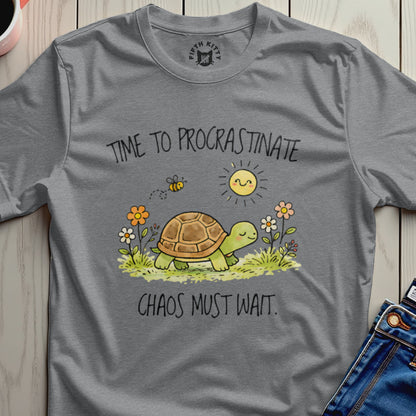 Grey t-shirt with a turtle, sun, bee, and flowers with text "TIME TO PROCRASTINATE. CHAOS MUST WAIT."