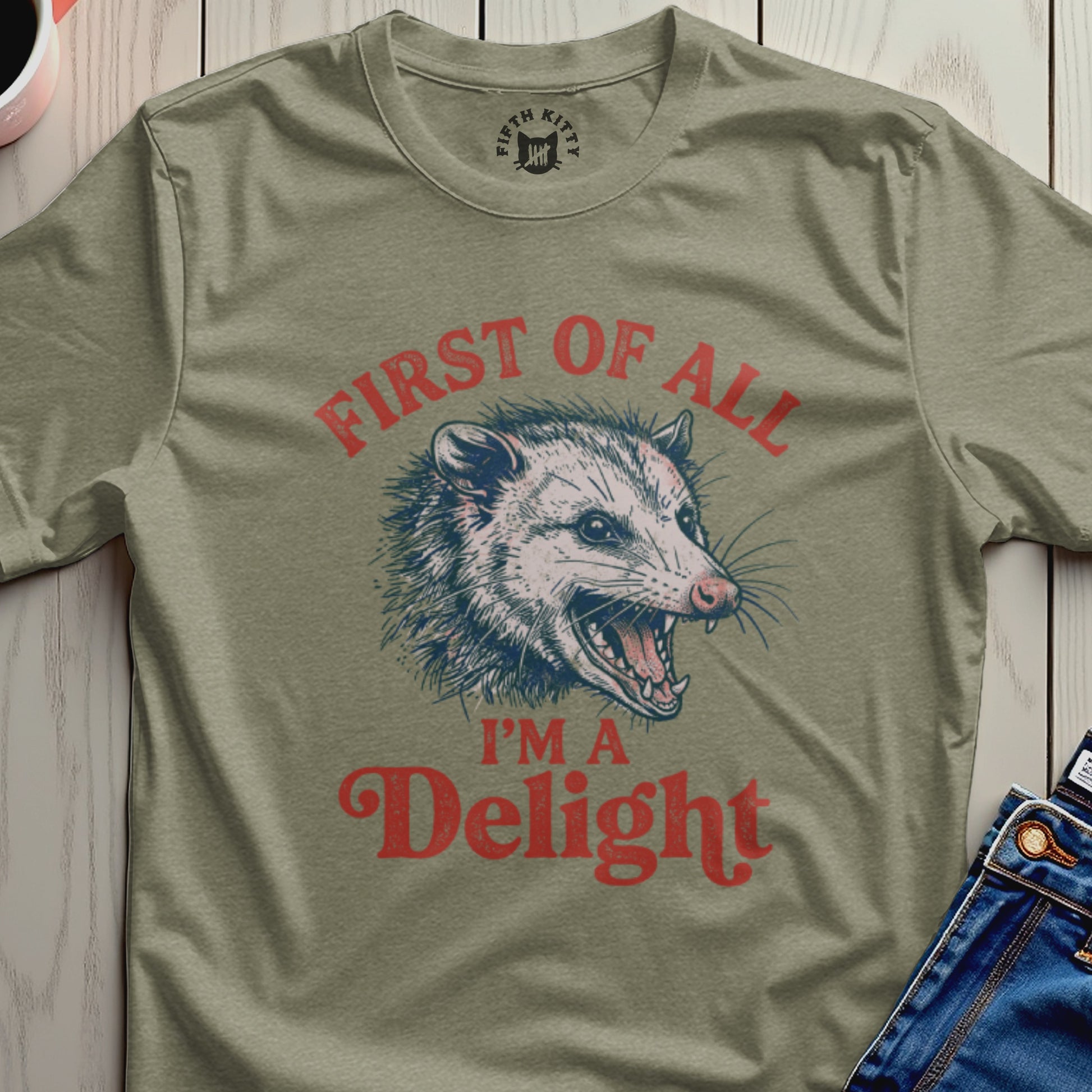 Olive green t-shirt with a graphic of a grinning opossum and text "First of all I'm a Delight."