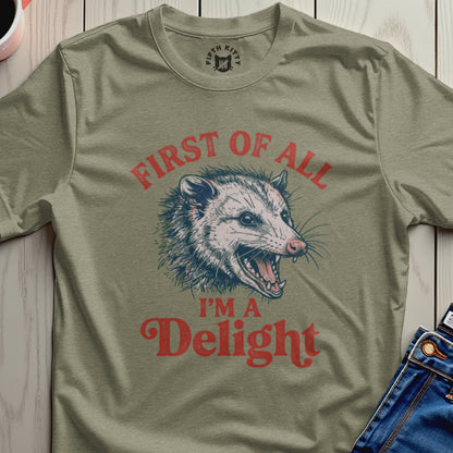 Olive green t-shirt with a graphic of a grinning opossum and text "First of all I'm a Delight."