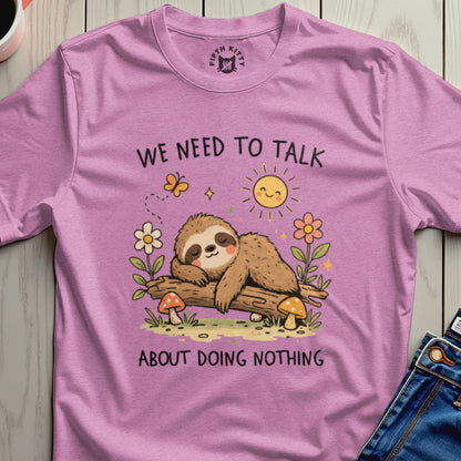 Pink t-shirt with a sleeping sloth, sun, and mushrooms saying "We need to talk about doing nothing."