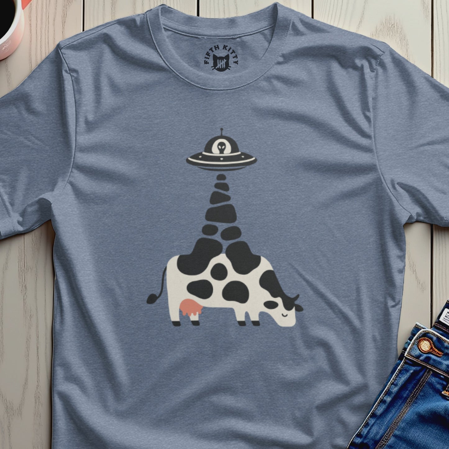Black and white cow with an alien spaceship beam on a blue t-shirt.