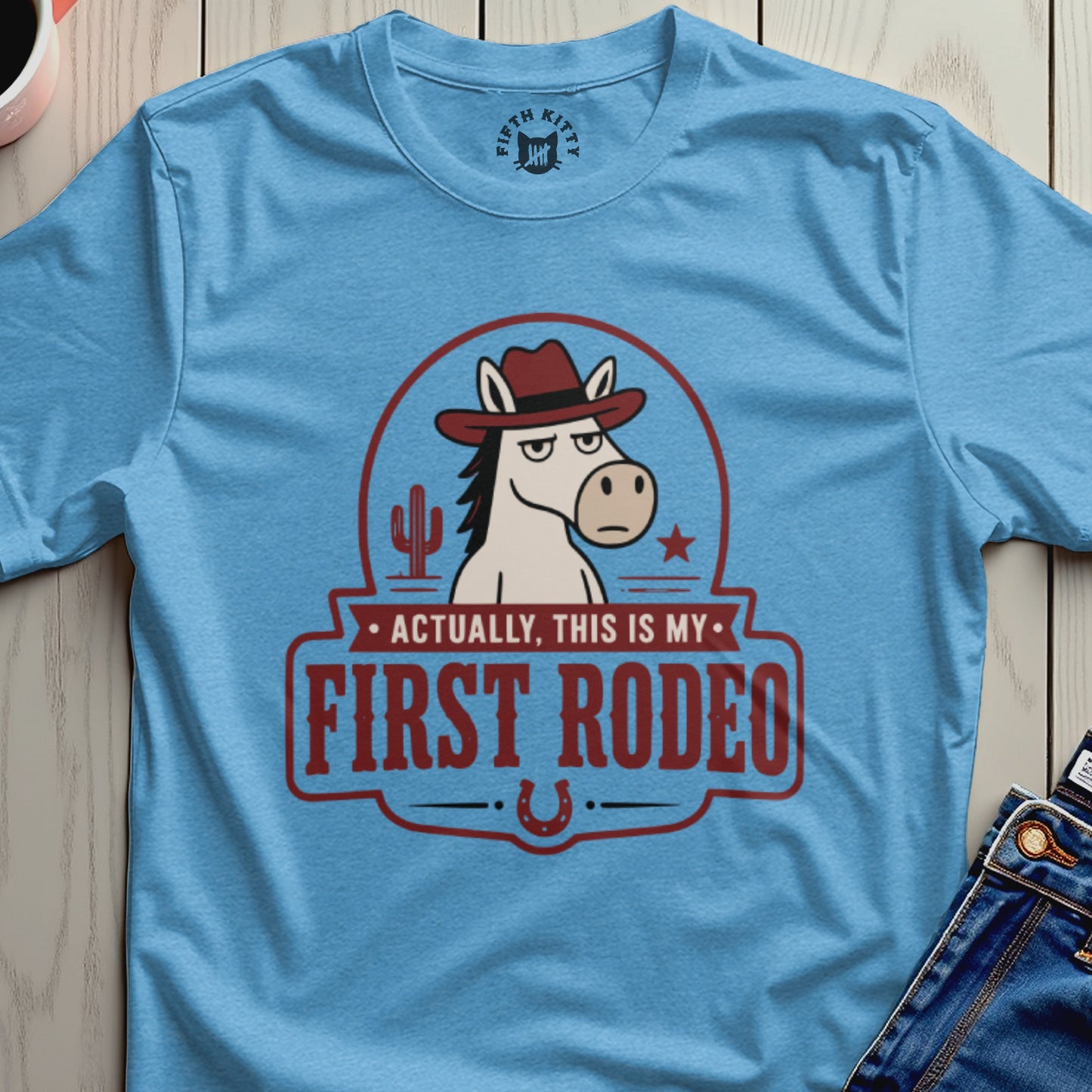 Light blue t-shirt with a cartoon horse wearing a cowboy hat and the text "Actually, This is My First Rodeo".