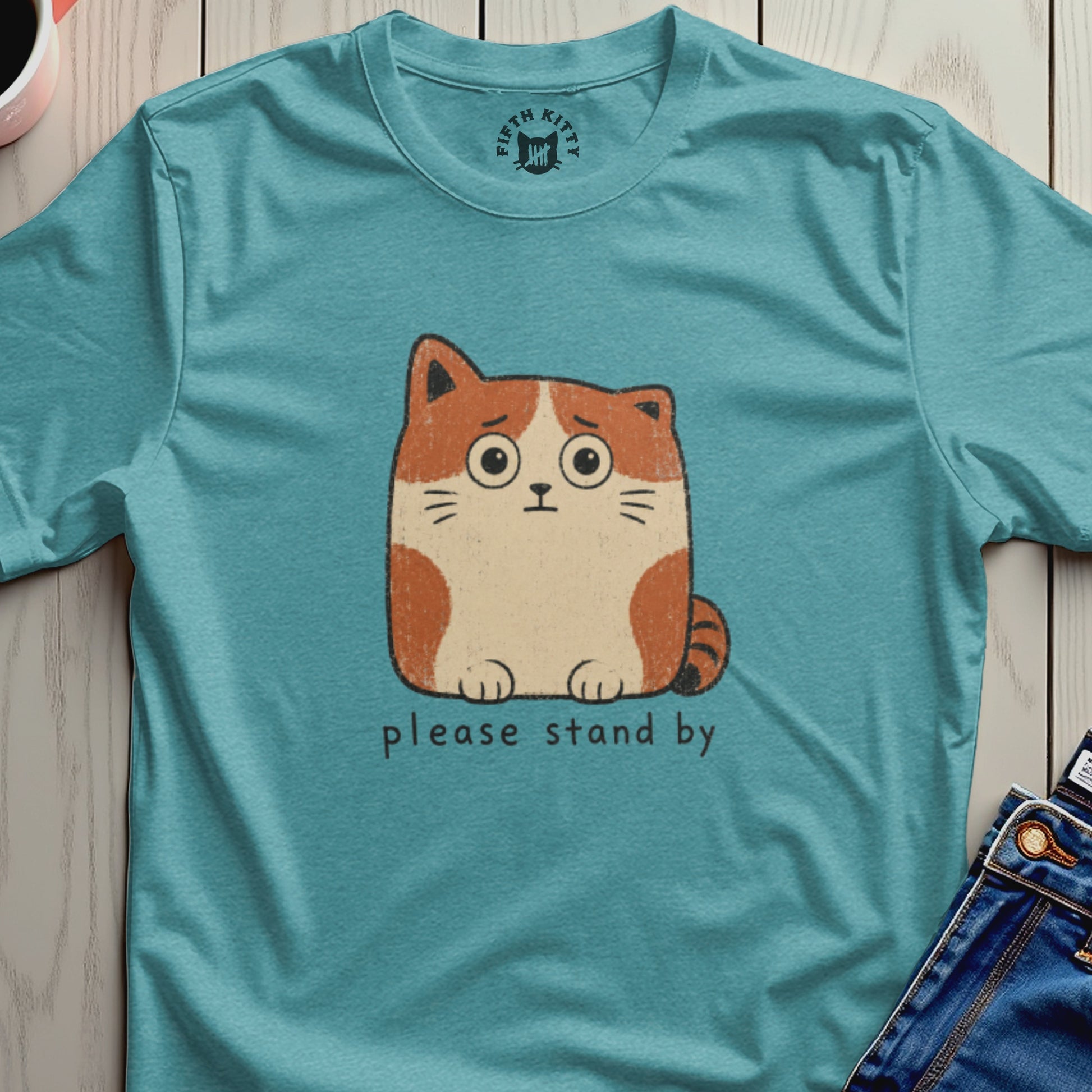 Teal t-shirt with a worried cartoon cat and "please stand by" text.