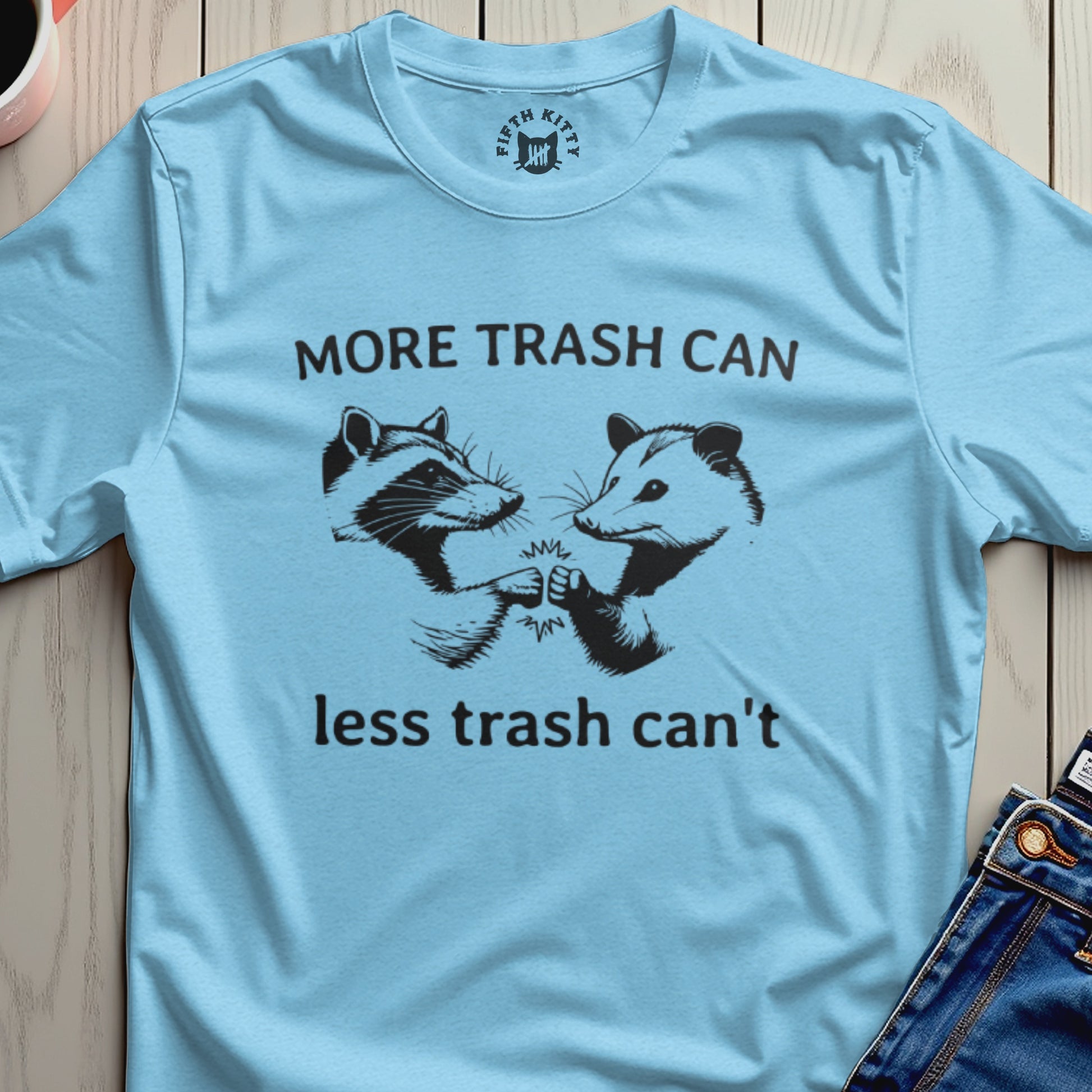 Light blue t-shirt with a raccoon and opossum fist-bumping, text reads "More Trash Can Less Trash Can't".