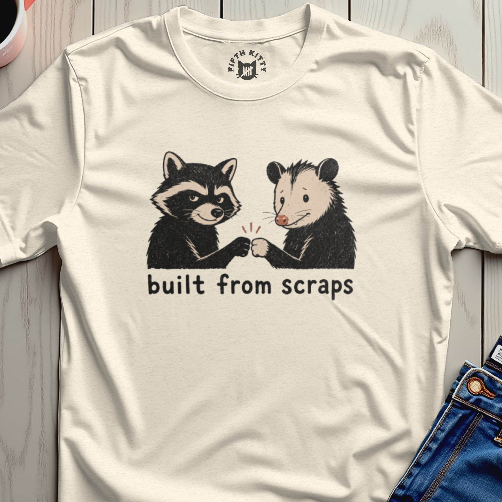Cream t-shirt with a raccoon and opossum giving a fist bump, text reads "built from scraps."