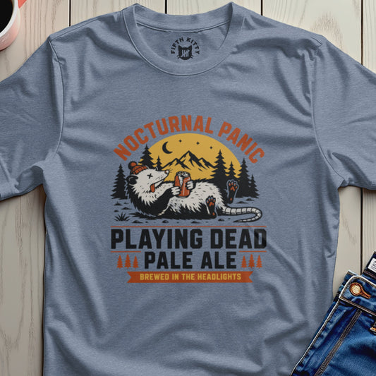Gray t-shirt with 'Nocturnal Panic Playing Dead Pale Ale' graphic on a wooden surface.