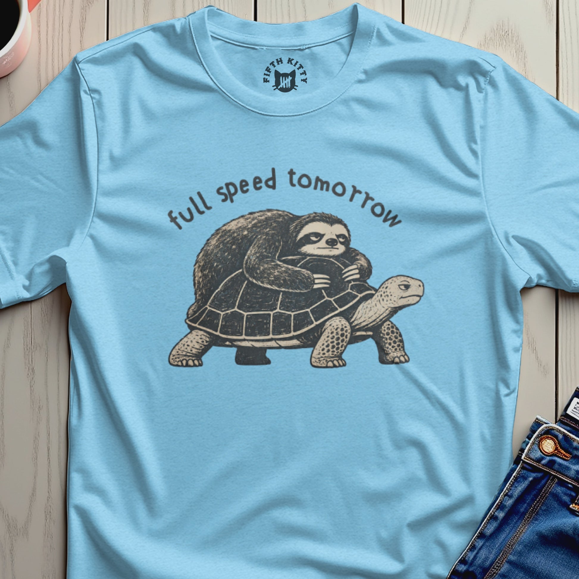 Light blue t-shirt with a sloth riding a turtle, text reads "full speed tomorrow."