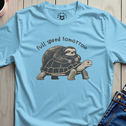 Light blue t-shirt with a sloth riding a turtle, text reads "full speed tomorrow."