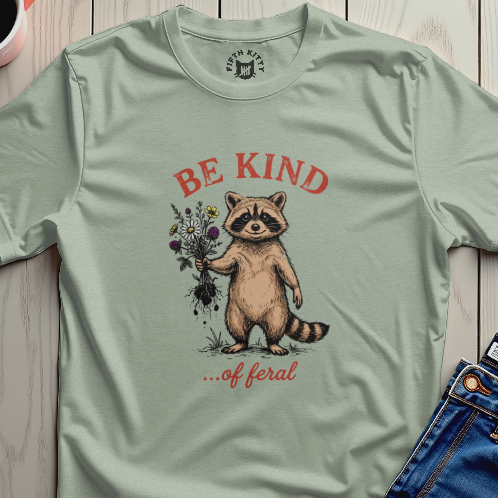 Raccoon holding flowers with text "BE KIND ...of feral" on a t-shirt.
