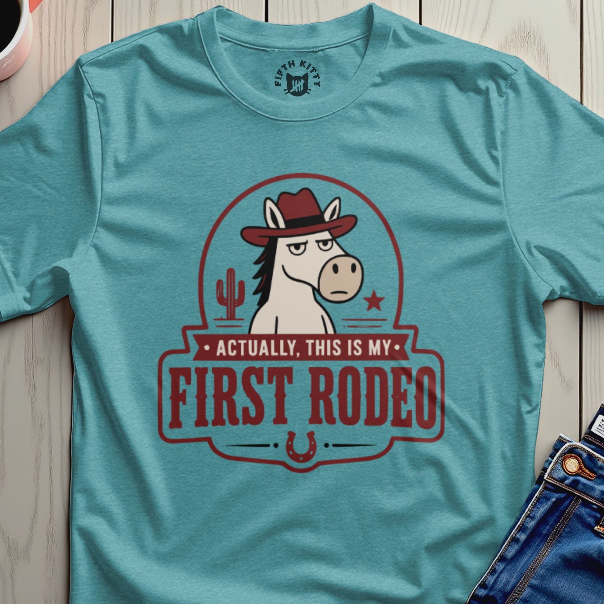 Turquoise t-shirt with a vintage-style graphic of a horse wearing a hat and the text "Actually, This Is My First Rodeo."