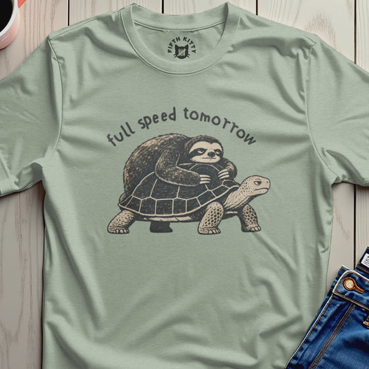Sloth riding a turtle with text "full speed tomorrow" on a sage green shirt.