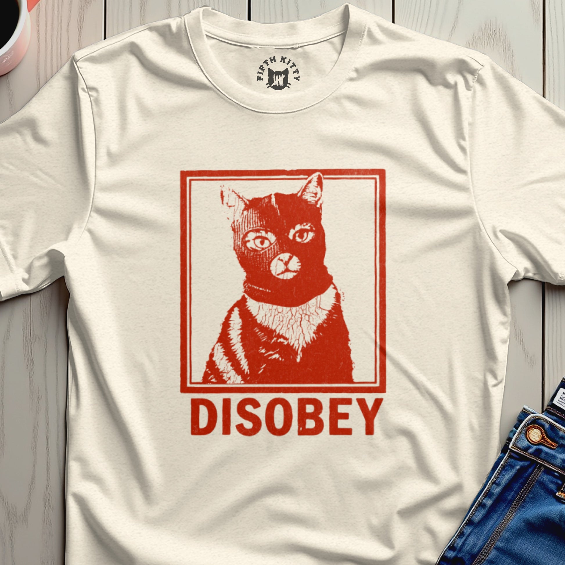 Cream t-shirt with a red graphic of a cat wearing a black ski mask and the word "DISOBEY".