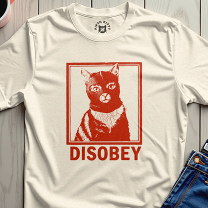 Cream t-shirt with a red graphic of a cat wearing a black ski mask and the word "DISOBEY".