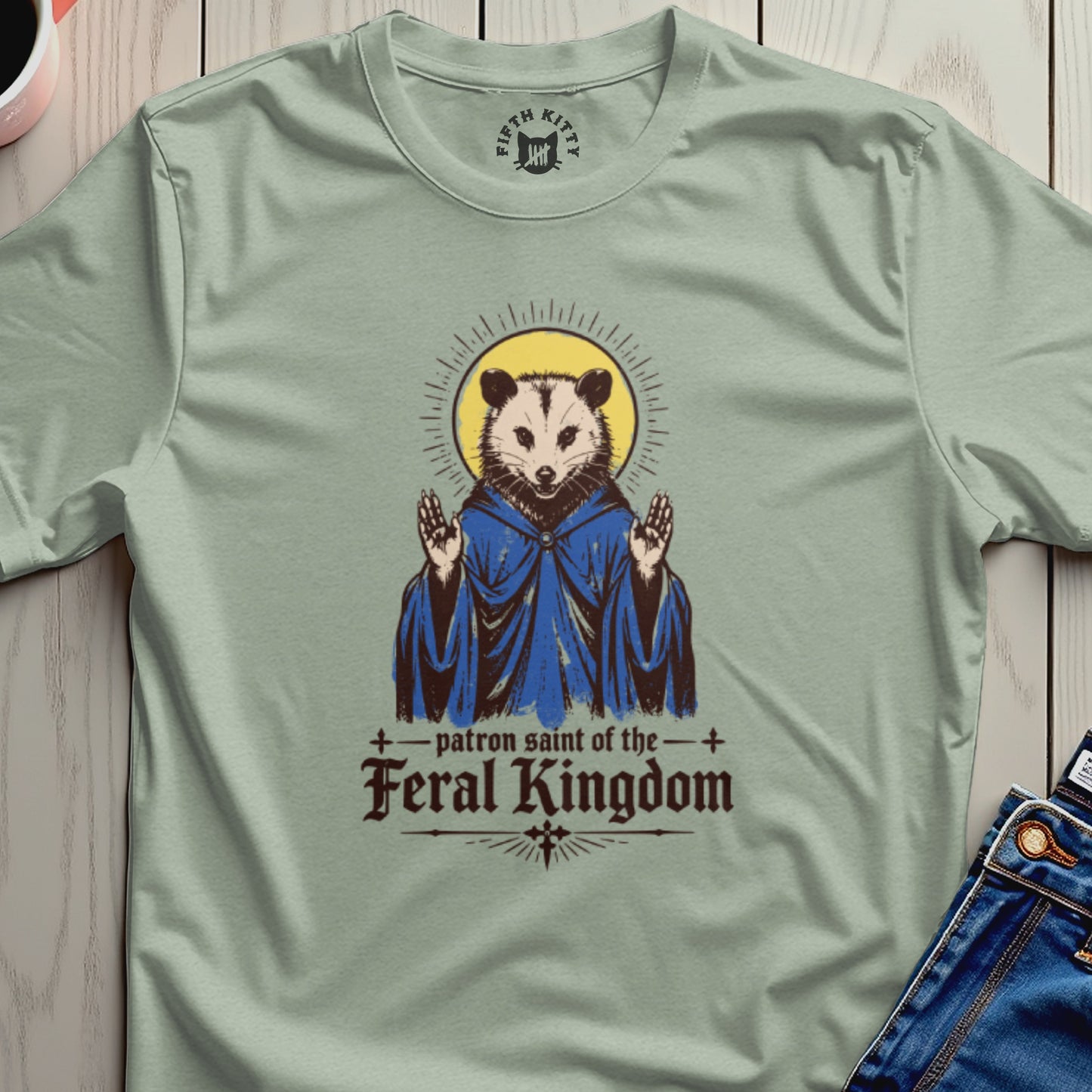 Saintly opossum in blue robe with "patron saint of the feral kingdom" text.