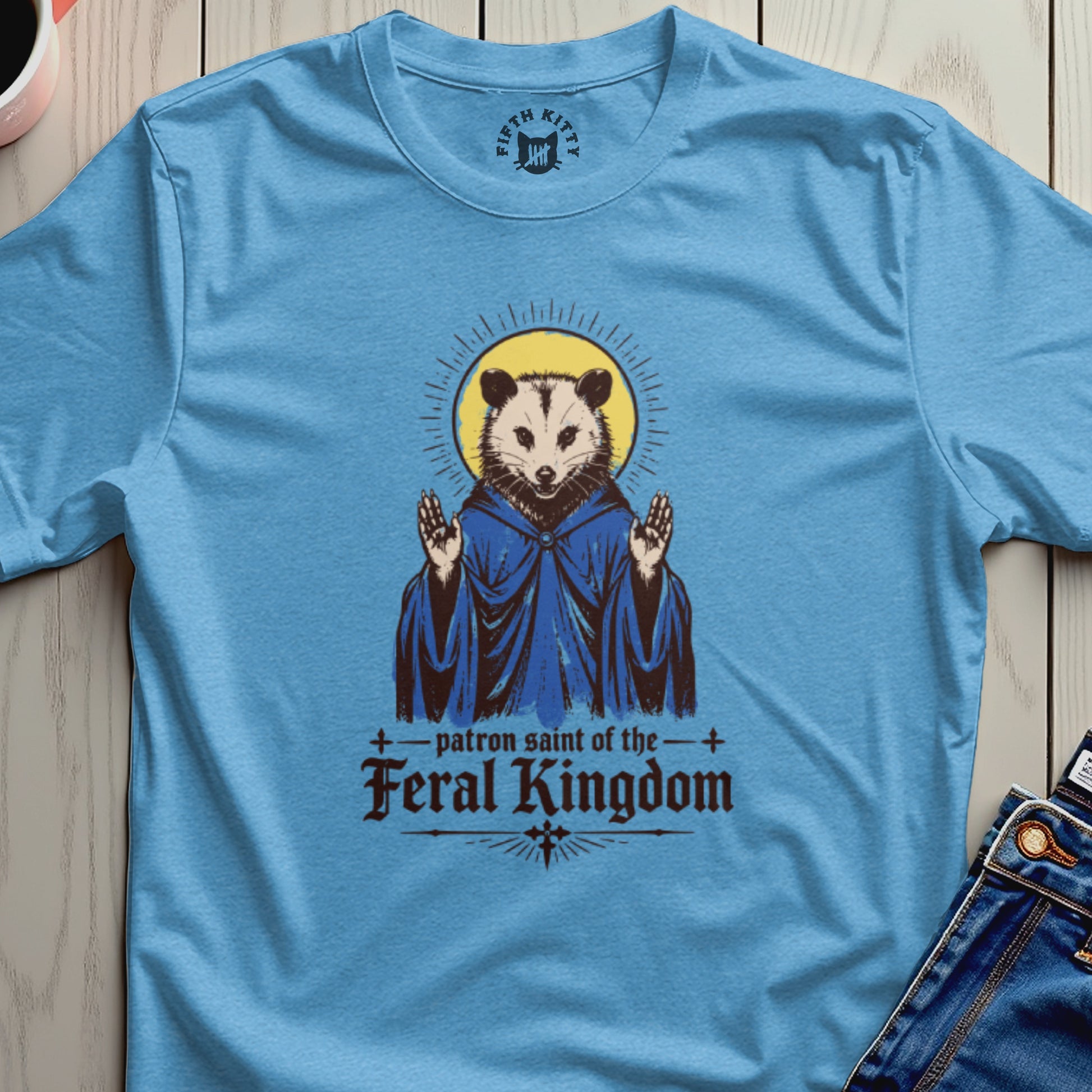 Opossum in blue robe with halo and text "patron saint of the Feral Kingdom".
