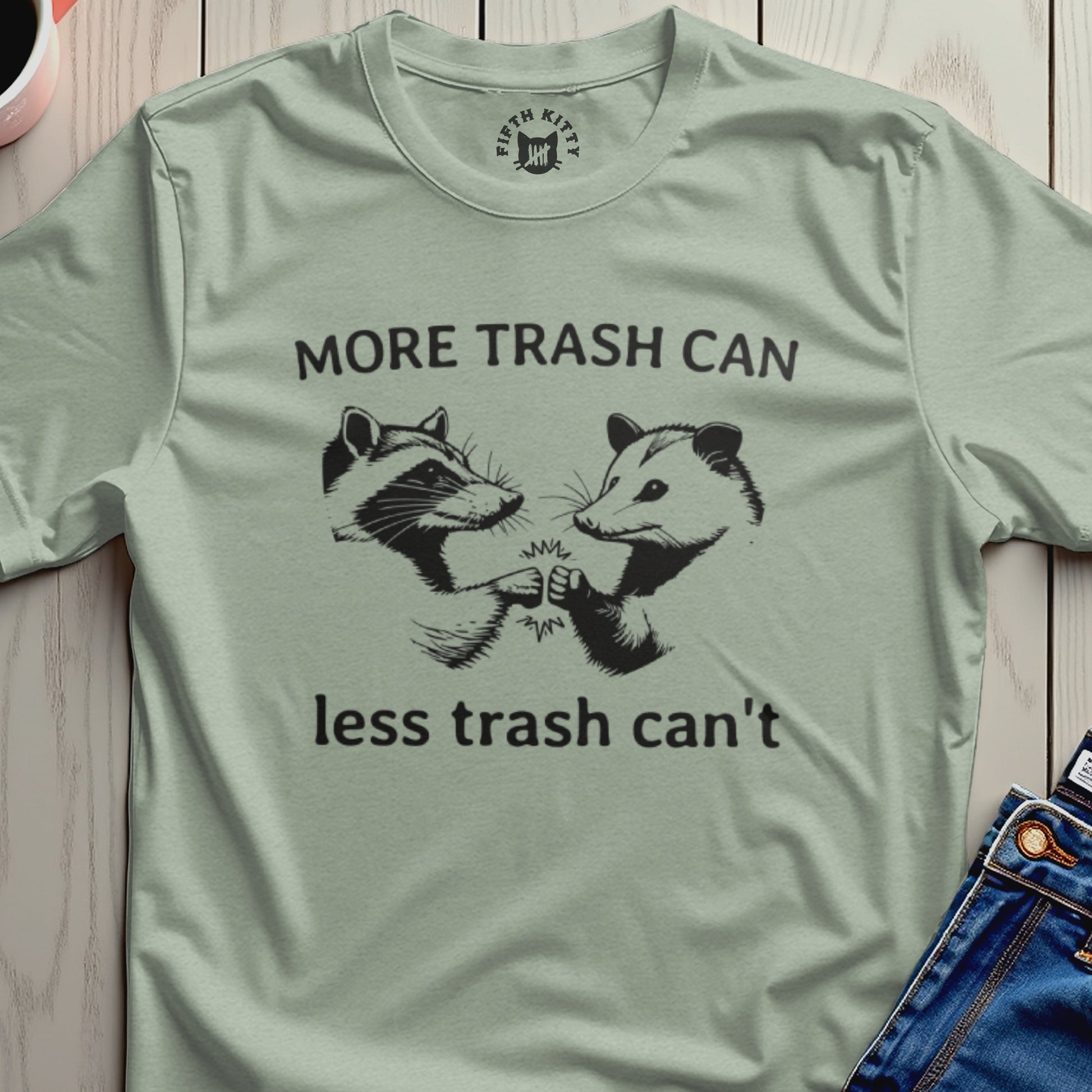 Light green t-shirt with raccoons and opossum fist-bumping, saying "More trash can, less trash can't".